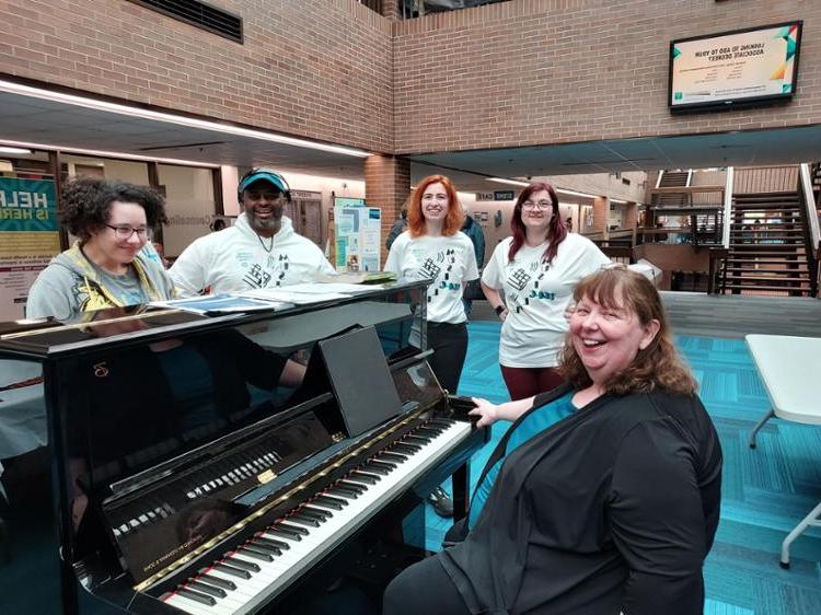 Tri-C West Campus Music Club members gathered around the piano in matching tee shirts